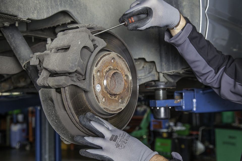 Gloved hands servicing a vehicle's disc brake rotor and caliper while the car sits on a lift at Johnny's Radiator and Auto Repair