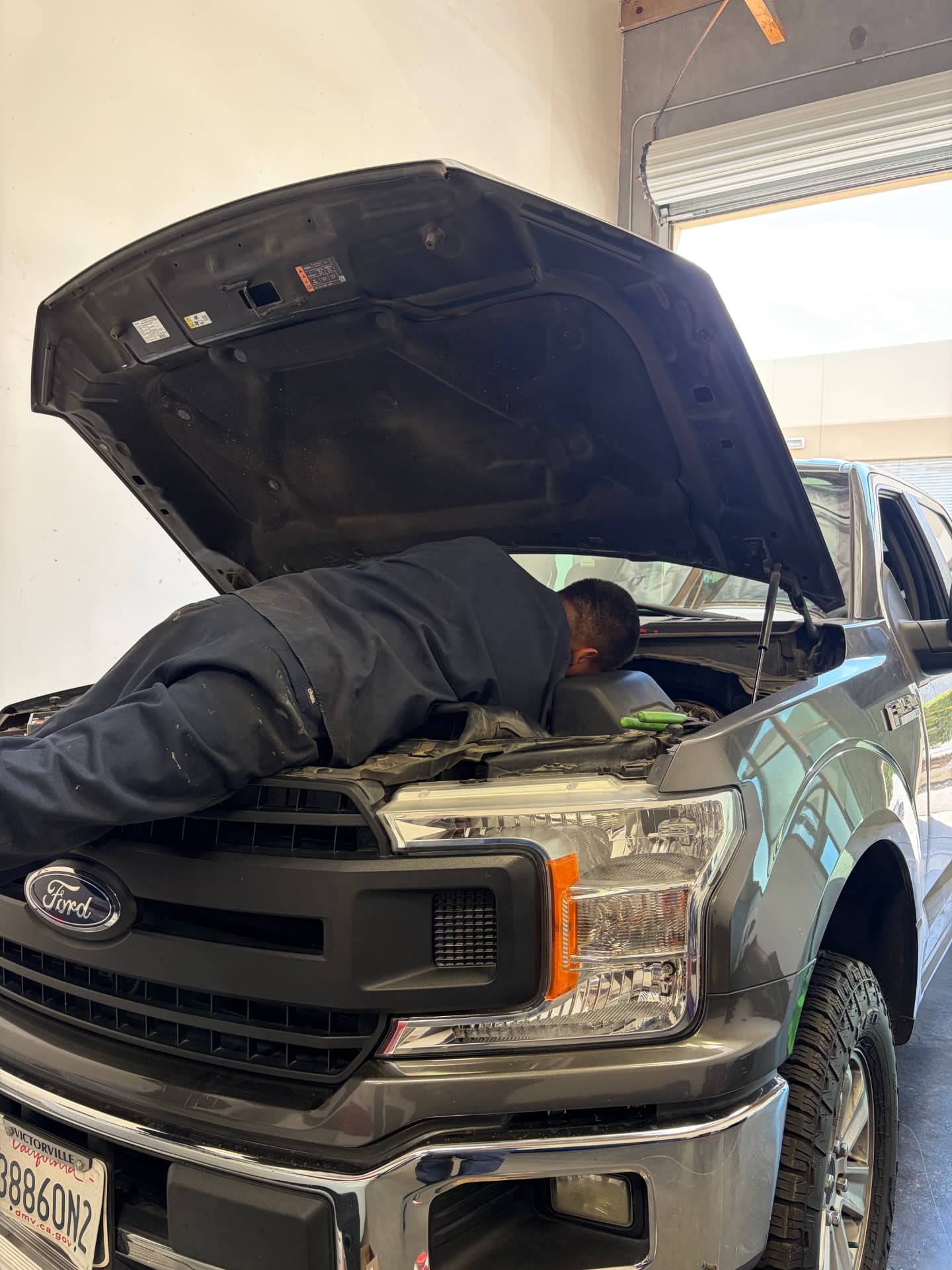 Mechanic working deep in the engine bay of a Ford F-150 at Johnny's Auto Repair in Victorville CA