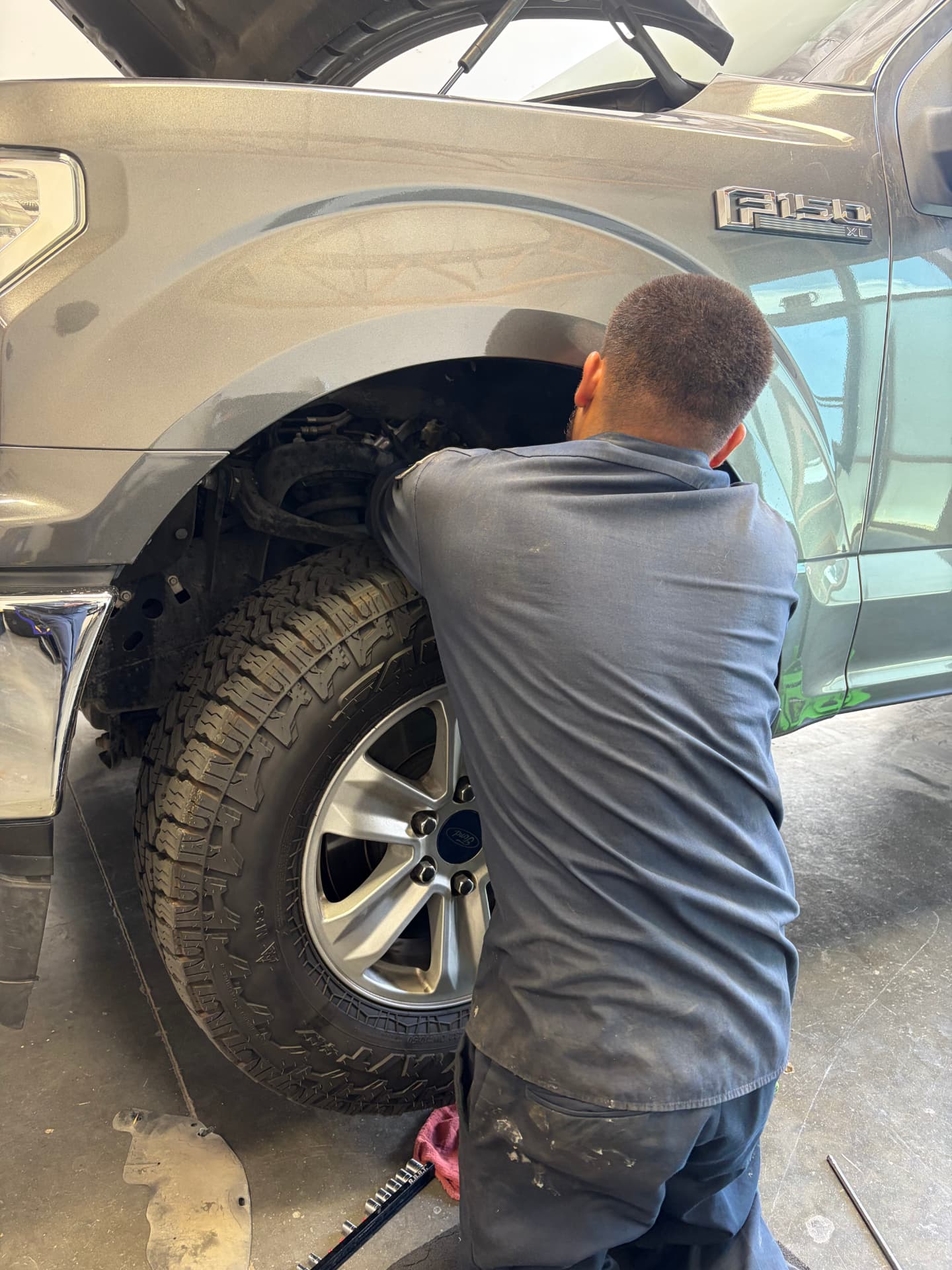 Mechanic repairing the front suspension and wheel well of a Ford F-150 at Johnny's Auto Repair in Victorville CA